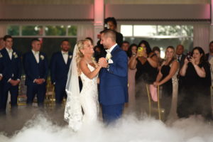 Newlyweds sharing their first dance on a cloud-covered dance floor under soft, romantic lighting.