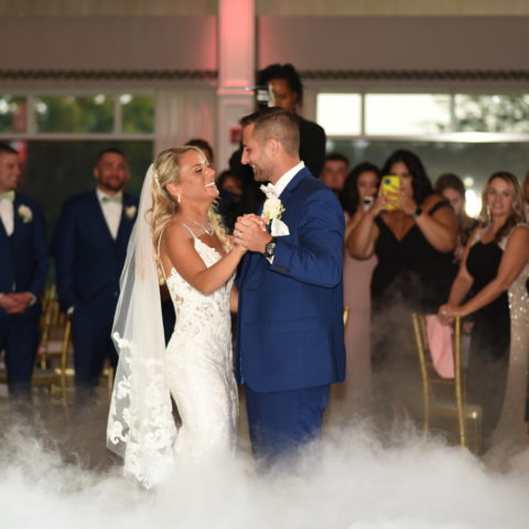 Newlyweds sharing their first dance on a cloud-covered dance floor under soft, romantic lighting.