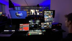 Technicians operating live streaming equipment and software behind the scenes at an event.