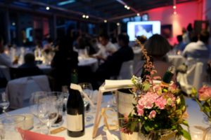 Close-up of an elegant table setting with flowers and wine bottles at a corporate gala dinner.