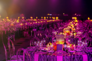 Rows of tables illuminated by purple lighting for a large corporate gala, creating a vibrant and stylish atmosphere.