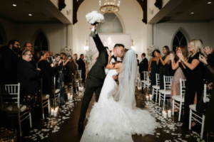 Bride and groom share a passionate first kiss at the altar, surrounded by wedding guests celebrating their union.