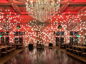 Wedding reception venue with dramatic lighting, chandeliers, and an open seating arrangement.
