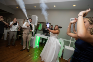 Bride and groom celebrating with their local DJ using fog effects and vibrant lighting at a wedding reception.