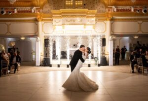 Bride and groom share a kiss on a white dance floor surrounded by cold sparkler effects.