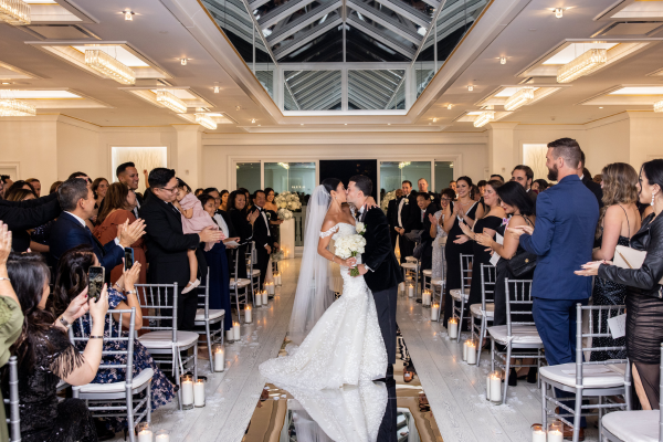 A bride and groom kiss during their indoor ceremony surrounded by family and friends.